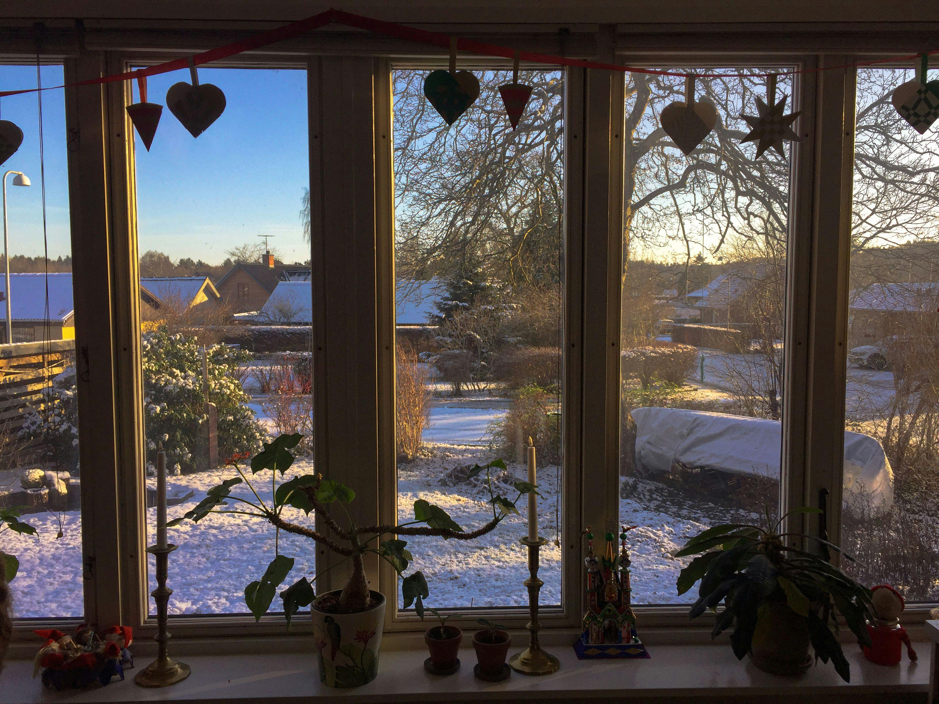A window overlooking the garden reveals snow-covered houses adorned with star and heart-shaped Christmas decorations